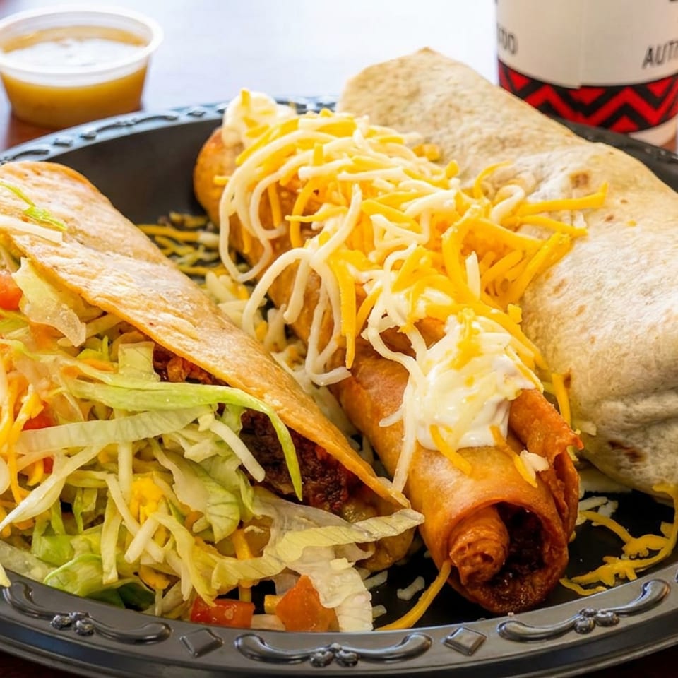 Black plate with a crunchy taco, two cheese-topped taquitos, a burrito, and dipping sauces.