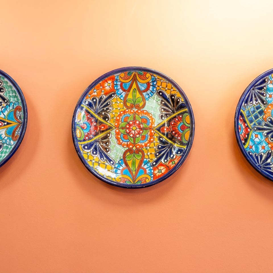 Three colorful, intricately patterned ceramic plates hang against a warm terracotta wall.